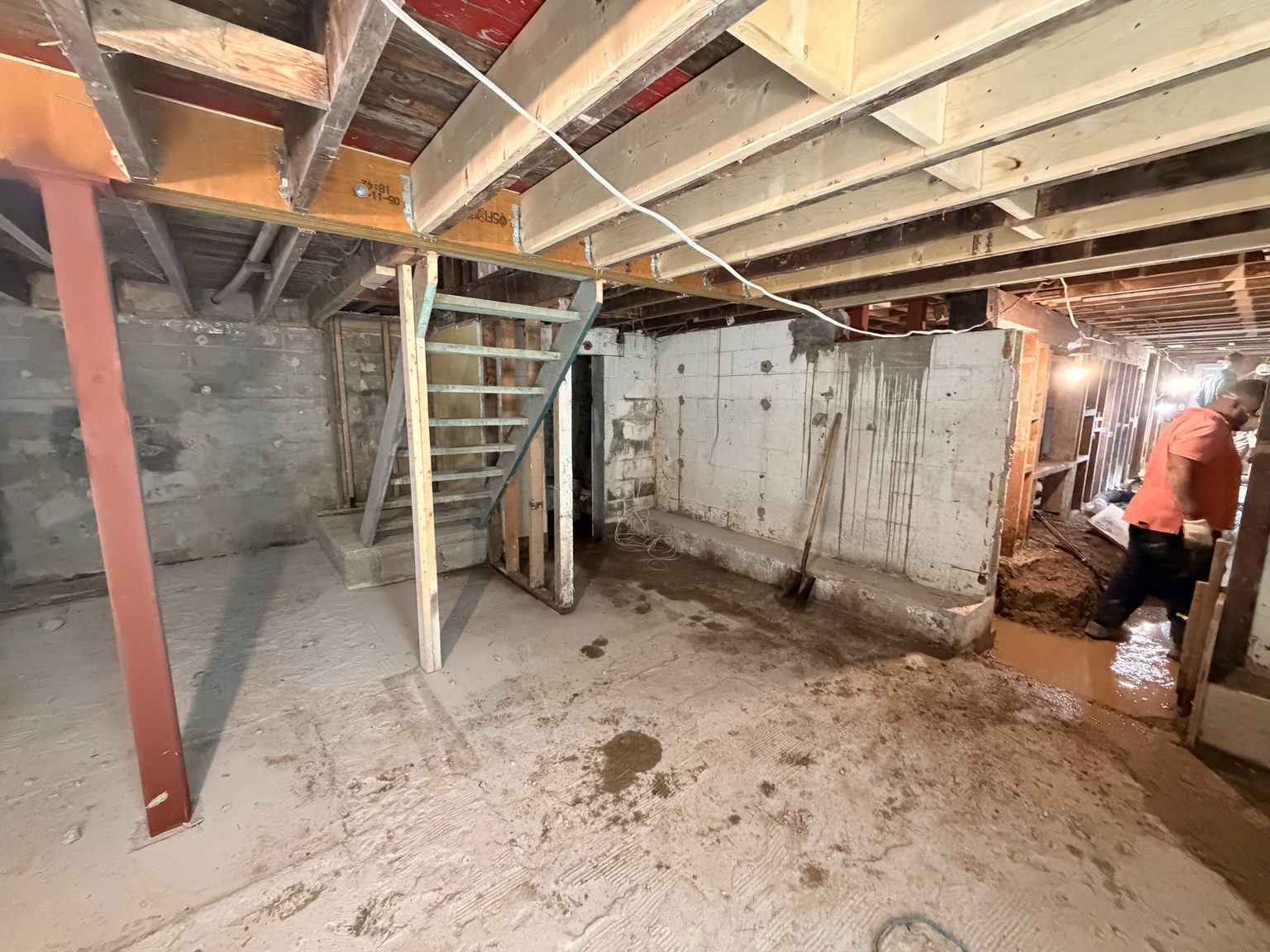 The basement with newly installed red steel posts and a beam carrying new floor joists overhead.
