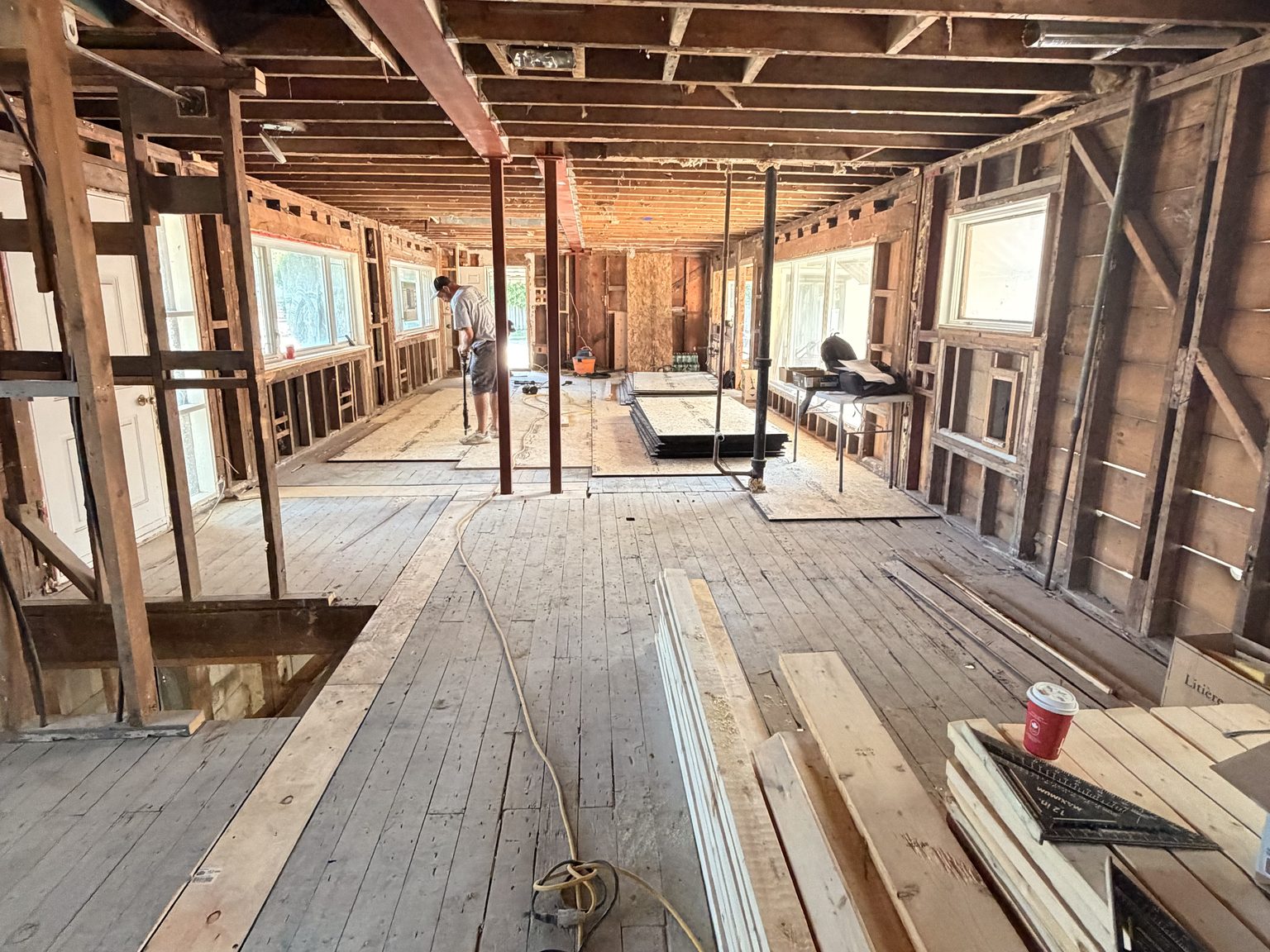 The full depth of the building seen end to end, original floorboards still down, new steel posts in place and daylight coming from windows on both sides.