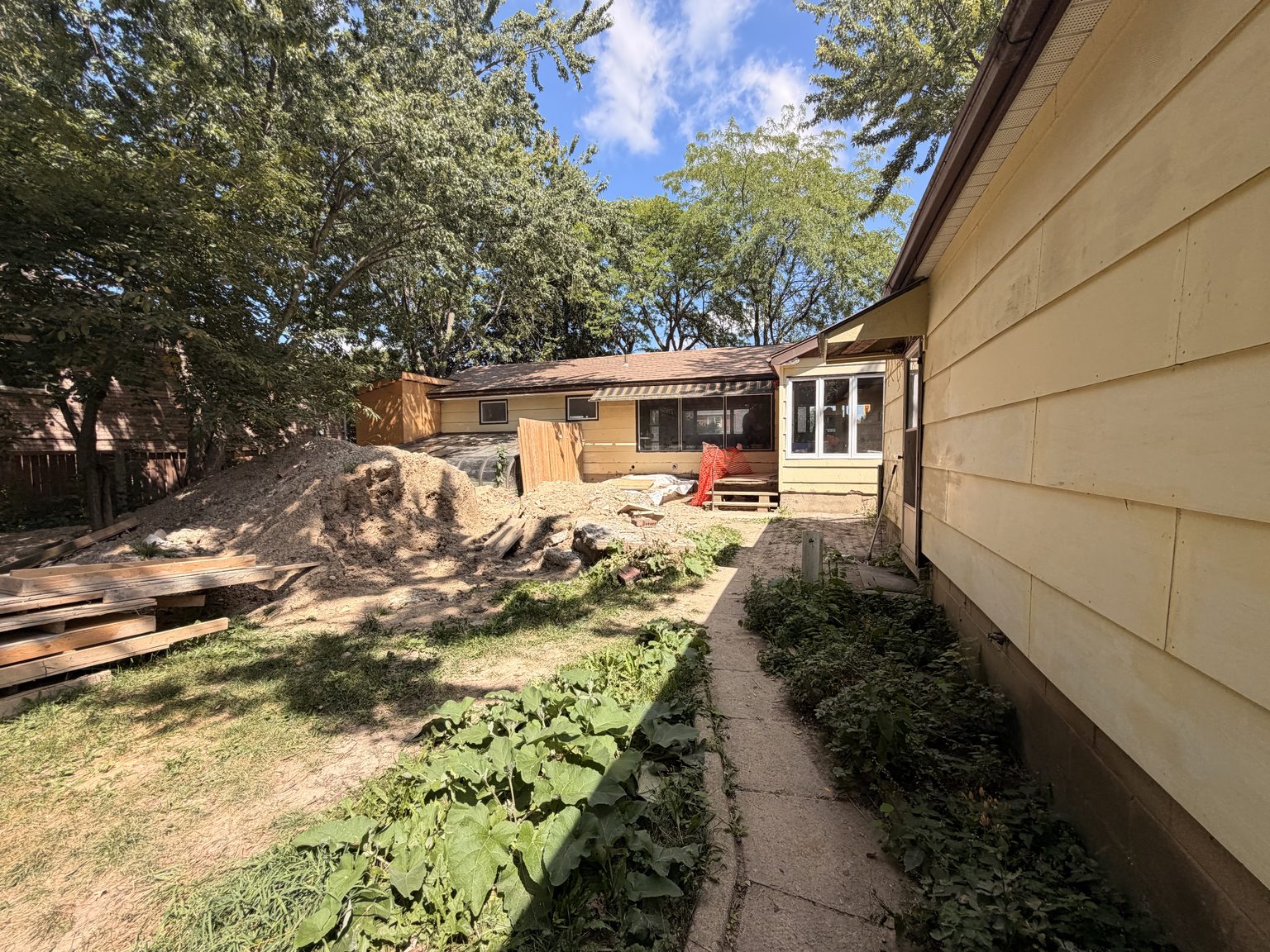 A concrete path running down the side of the building past mature trees, toward the open, treed rear of the lot.